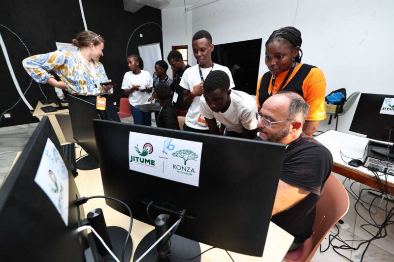 Group of students gather around a mentor at a computer during a coding workshop.