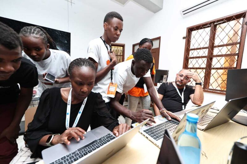 Young participants and mentors collaborate closely on laptops during a training session.