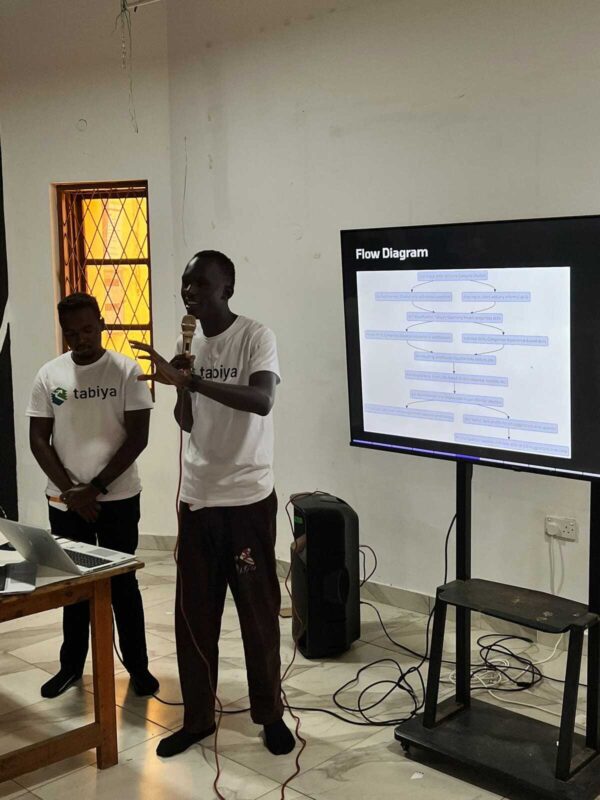 Two presenters explain a flow diagram displayed on a large screen.