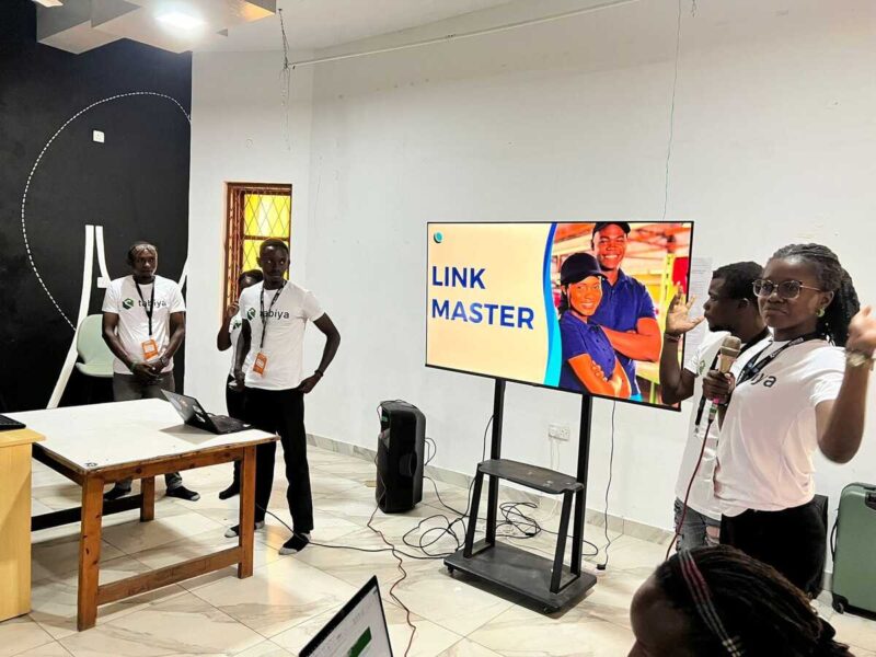 Participants stand by a screen showing "Link Master" during a demo presentation.