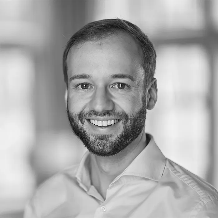 Professional black-and-white headshot of a smiling man with beard and collared shirt.