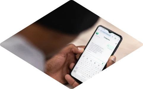 Person holding a smartphone using the Compass chatbot app, with a conversation visible on screen.