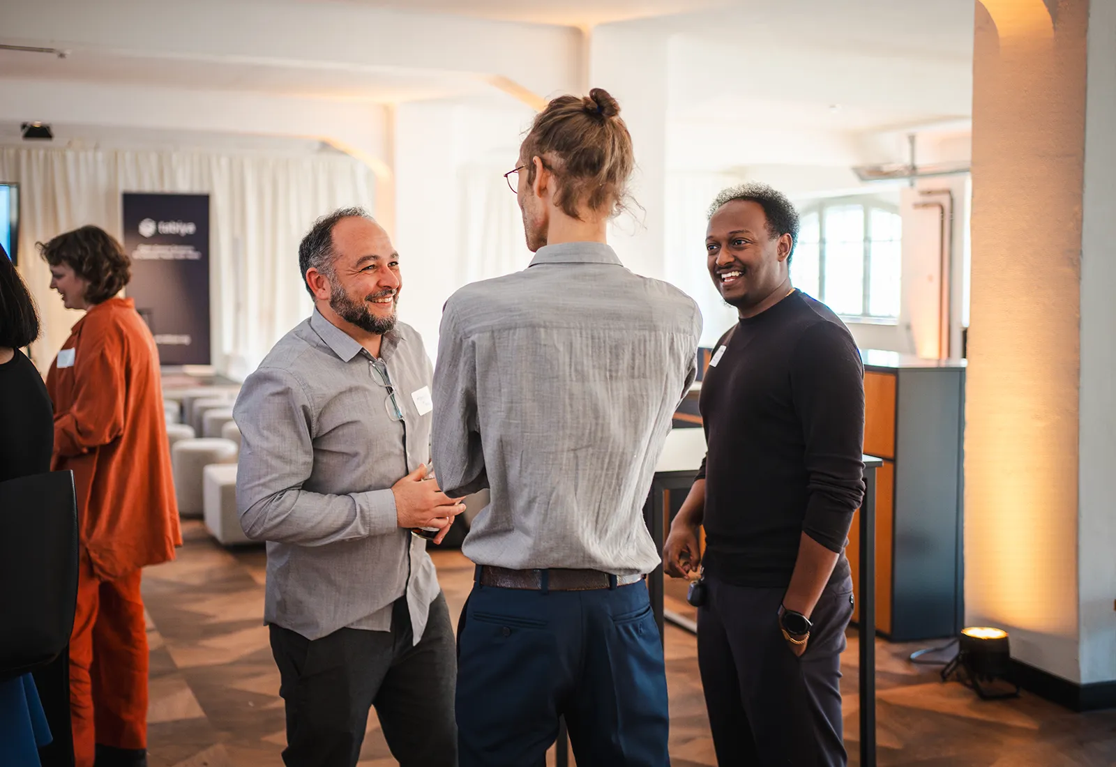 Three men have an informal conversation in a bright, open conference room.