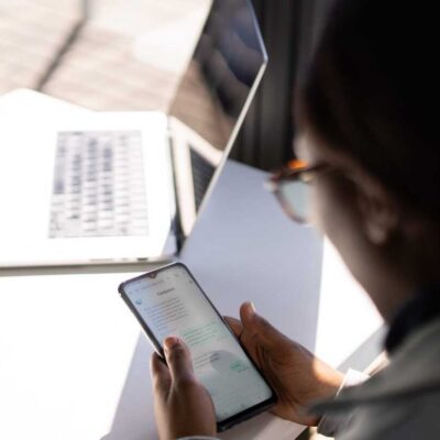 Woman using Compass chatbot app on a phone while working at a laptop.