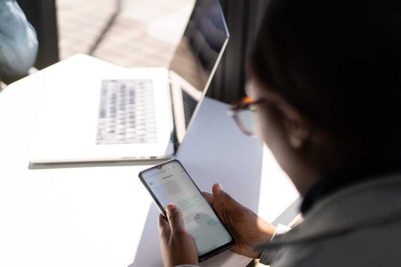 Woman using Compass chatbot app on a phone while working at a laptop.