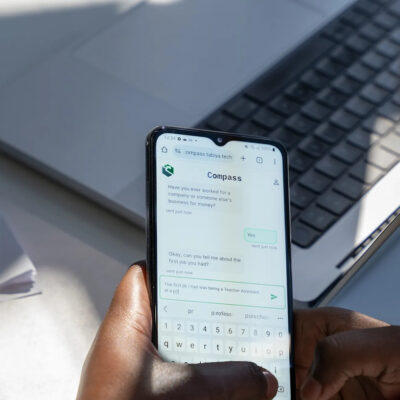 Woman using Compass chatbot app on a phone while working at a laptop.